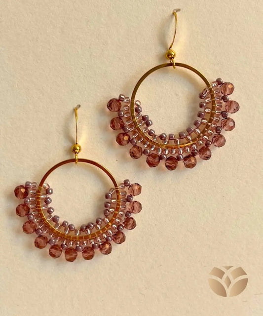 Aros tejidos con técnica Peyote con cristales y mostacillas en tonos Lila, de forma redondeada, base y gancho de acero inoxidable.