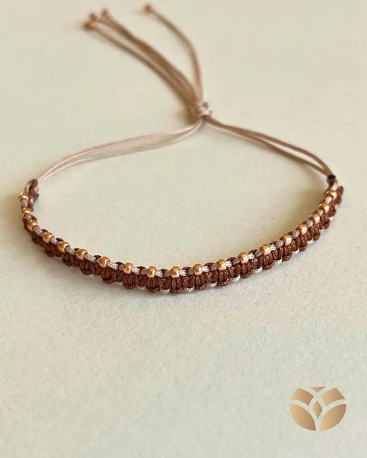 Pulsera tejida con técnica macramé, combina nudo plano con nudo alondra, en tonos café y beige, lleva a un lado mostacillas doradas para resaltar la belleza del tejido. Es ajustable a cualquier muñeca.