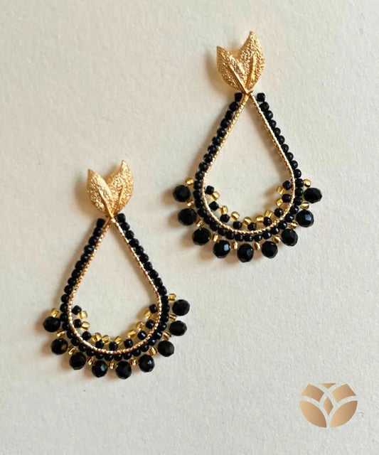 Aros en forma de gota,  tejidos con técnica peyote en mostacillas negras y doradas y cristales negros, base y gancho en acero inixidable. 