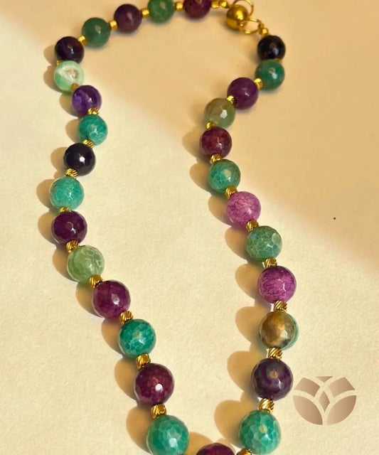  Elaborado con piedras naturales de ágata en tonos morado profundo y verde agua, incorpora en el diseño delicados balines dorados entre cada piedra que aportan sofisticación, mientras que su cierre imantado lo hace práctico y seguro de llevar en cualquier ocasión. 