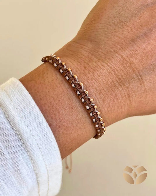 Pulsera tejida con técnica macramé, combina nudo plano con nudo alondra, en tonos café y beige, lleva a un lado mostacillas doradas para resaltar la belleza del tejido. Es ajustable a cualquier muñeca.