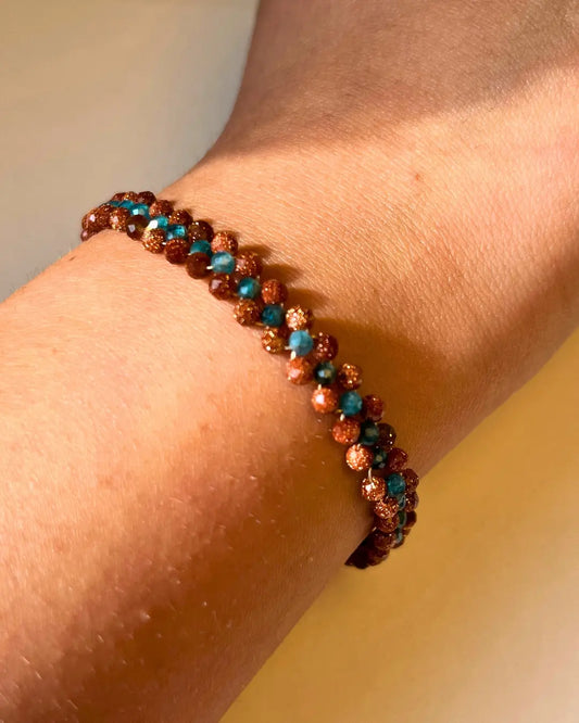 Pulsera tejida que lleva dos piedras, Apatita color azul con toques claros y piedra del sol color bronce con puntos brillantes.
