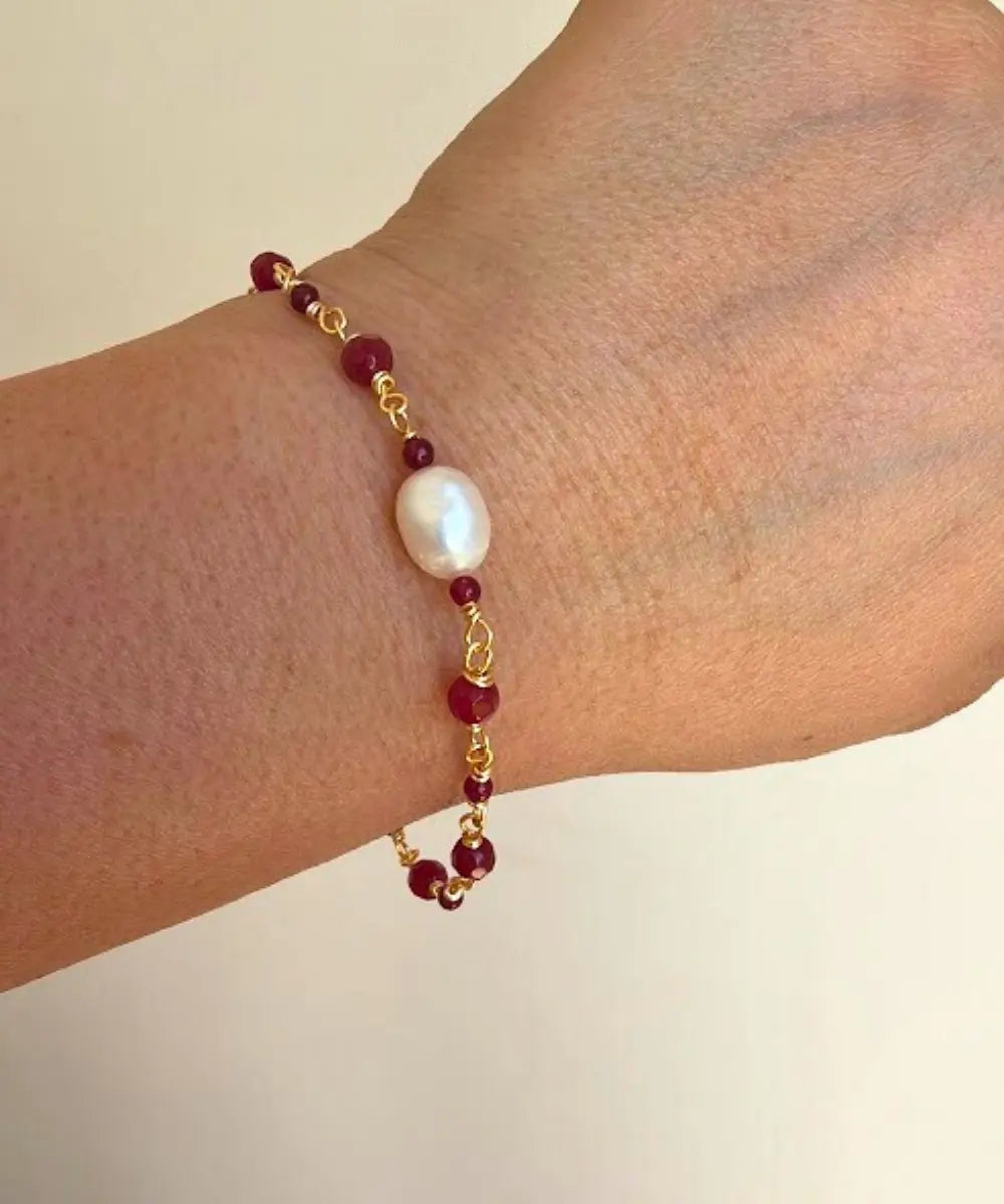 Entorchada a mano en piedra ágata burdeo, esta hermosa pulsera lleva al centro una Perla de Río.