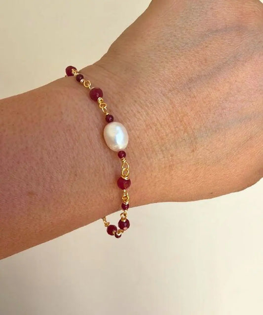 Entorchada a mano en piedra ágata burdeo, esta hermosa pulsera lleva al centro una Perla de Río.