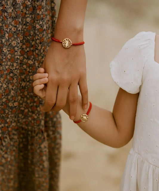 Pulsera tejida con técnica macramé con medalla de la virgen, en tono rojo, en la imagen se aprecia a una madre y su hija