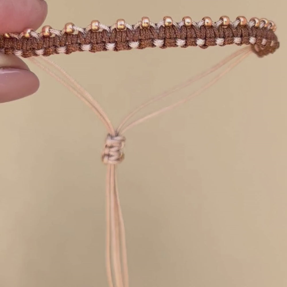 Pulsera tejida con técnica macramé, combina nudo plano con nudo alondra, en tonos café y beige, lleva a un lado mostacillas doradas para resaltar la belleza del tejido. Es ajustable a cualquier muñeca.