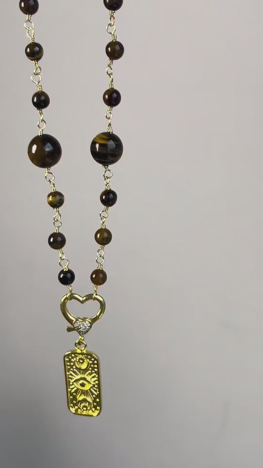 Está elaborado con piedras naturales Ojo de Tigre , cuidadosamente entorchadas para resaltar sus tonos dorados y marrones únicos.
En el centro, un broche en forma de corazón sostiene un dije dorado grabado con símbolos , que aporta un aire cómodo y distintivo.